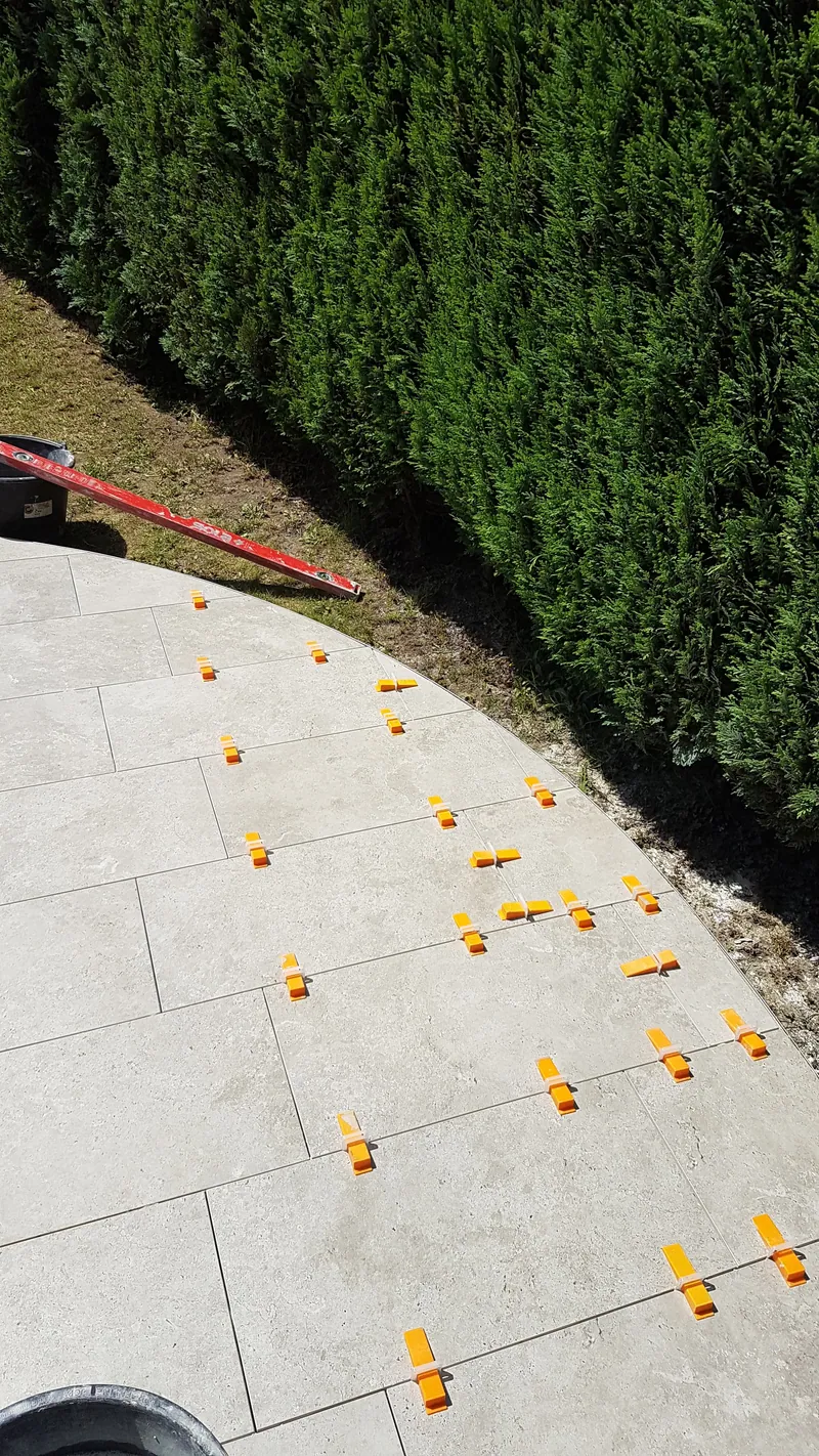 Terrasse mit frisch verlegten hellen Fliesen und Nivellierklammern an einer Hecke