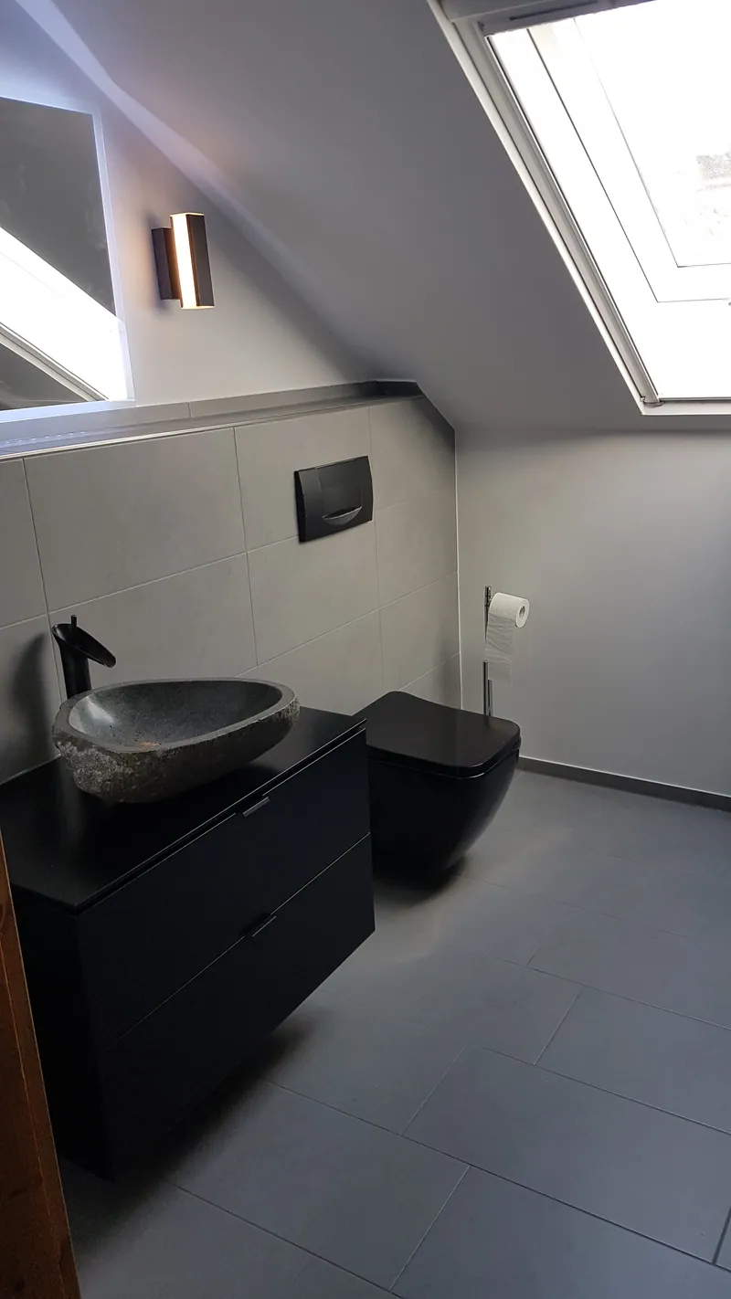 Saniertes Bad im Dachgeschoss mit grauen Bodenfliesen, Steinwaschbecken und Wand-WC