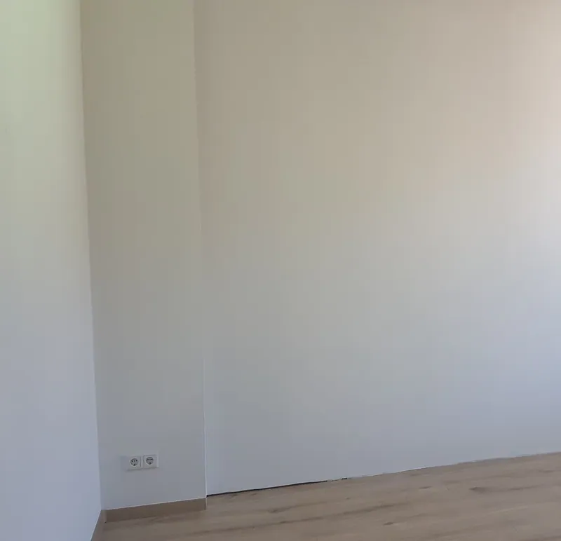 Frisch gestrichene weiße Wand in einem leeren Zimmer mit Holzoptik-Boden