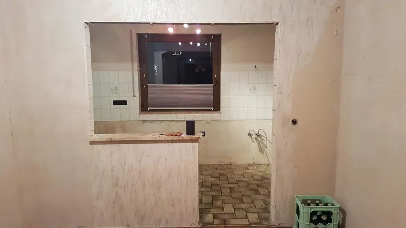 Entkernte Küche mit Wanddurchbruch, Fliesenresten und Mosaikboden