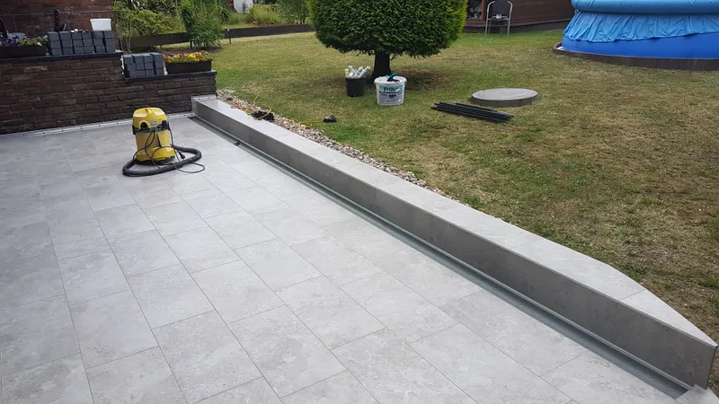 Fertig gefliestete Terrasse mit Randstein neben dem Rasen