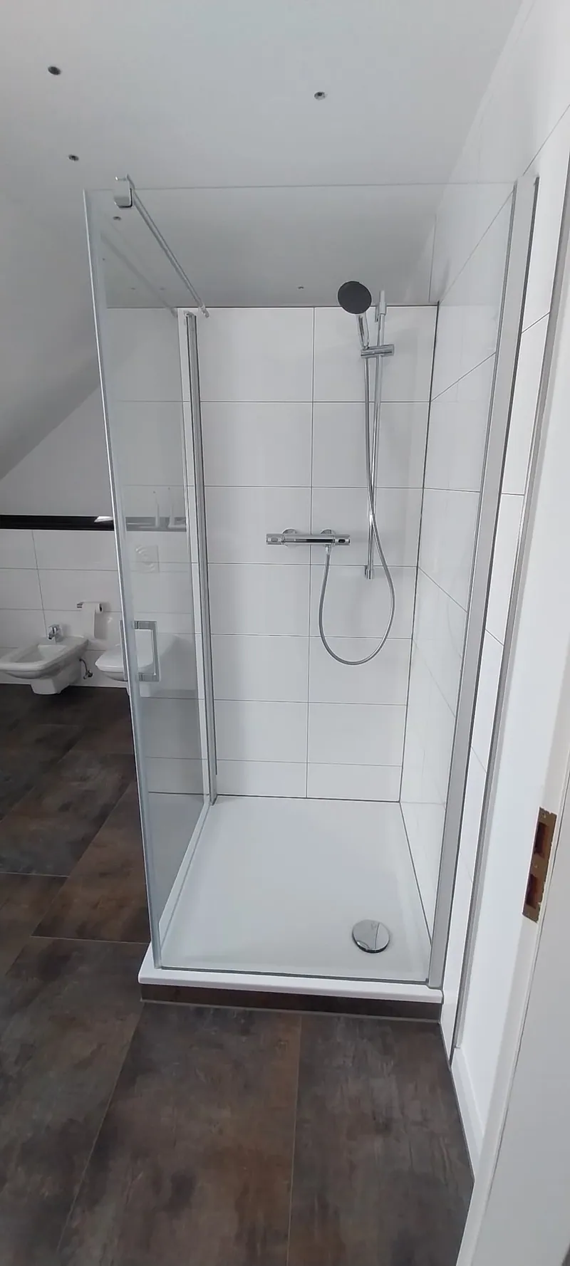 Dachgeschossbad mit weißer gefliester Duschkabine und dunklem Holzoptik-Boden