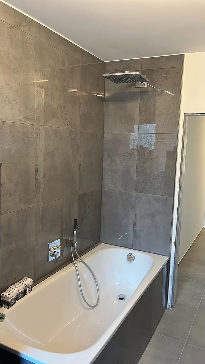 Badewanne mit Brausestange vor großformatigen braungrauen Wandfliesen