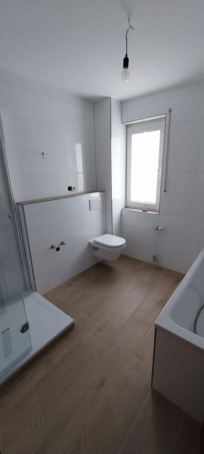 Bad mit weißen Wandfliesen, Eckdusche, Wand-WC und Holzoptik-Boden