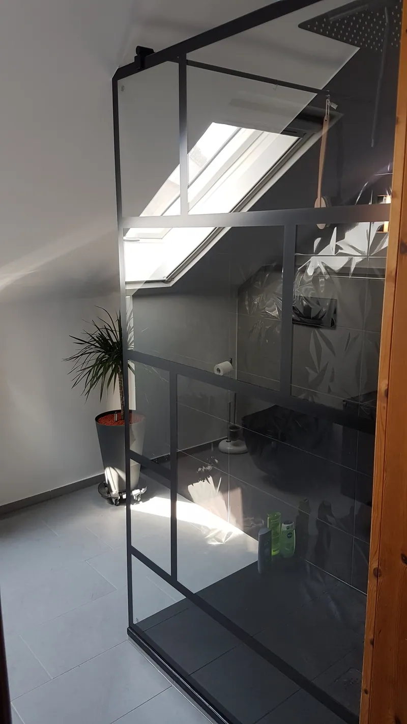 Dachgeschossbad mit schwarz gerahmter Glasdusche und hellgrauen Bodenfliesen