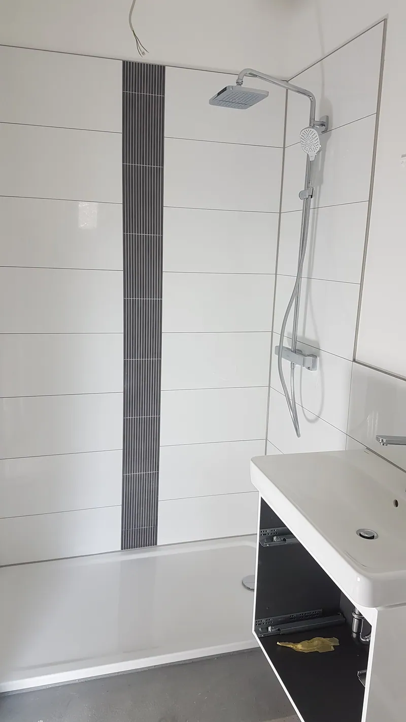 Dusche mit weißen Langformatfliesen, dunklem Fliesenstreifen und Waschtisch