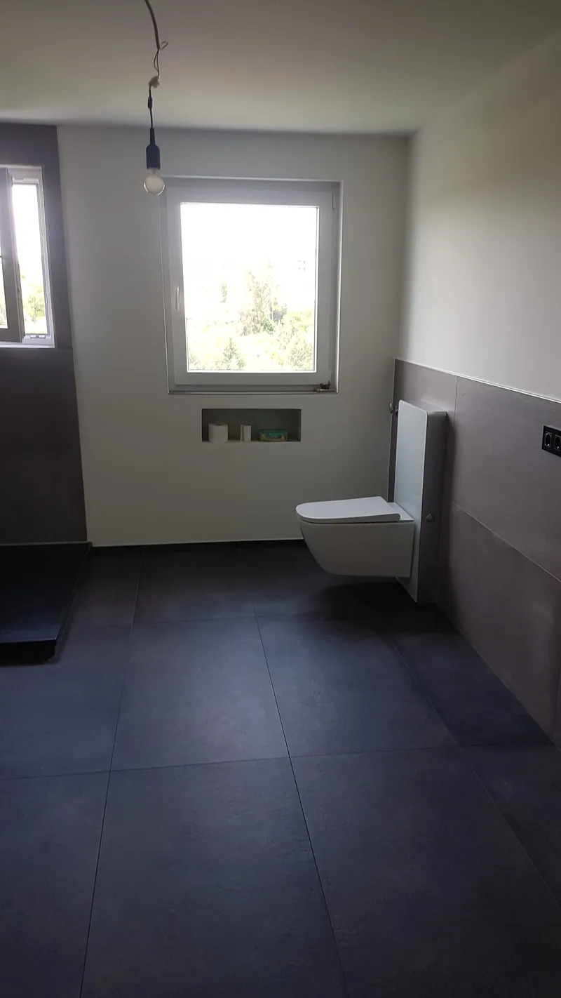 Bad mit dunklen großformatigen Bodenfliesen, grauen Wandfliesen und Wand-WC