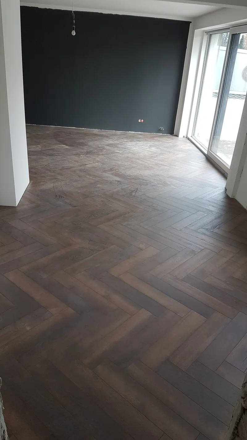 Wohnraum mit dunklen Holzoptik-Fliesen im Fischgrätmuster und dunkler Wand