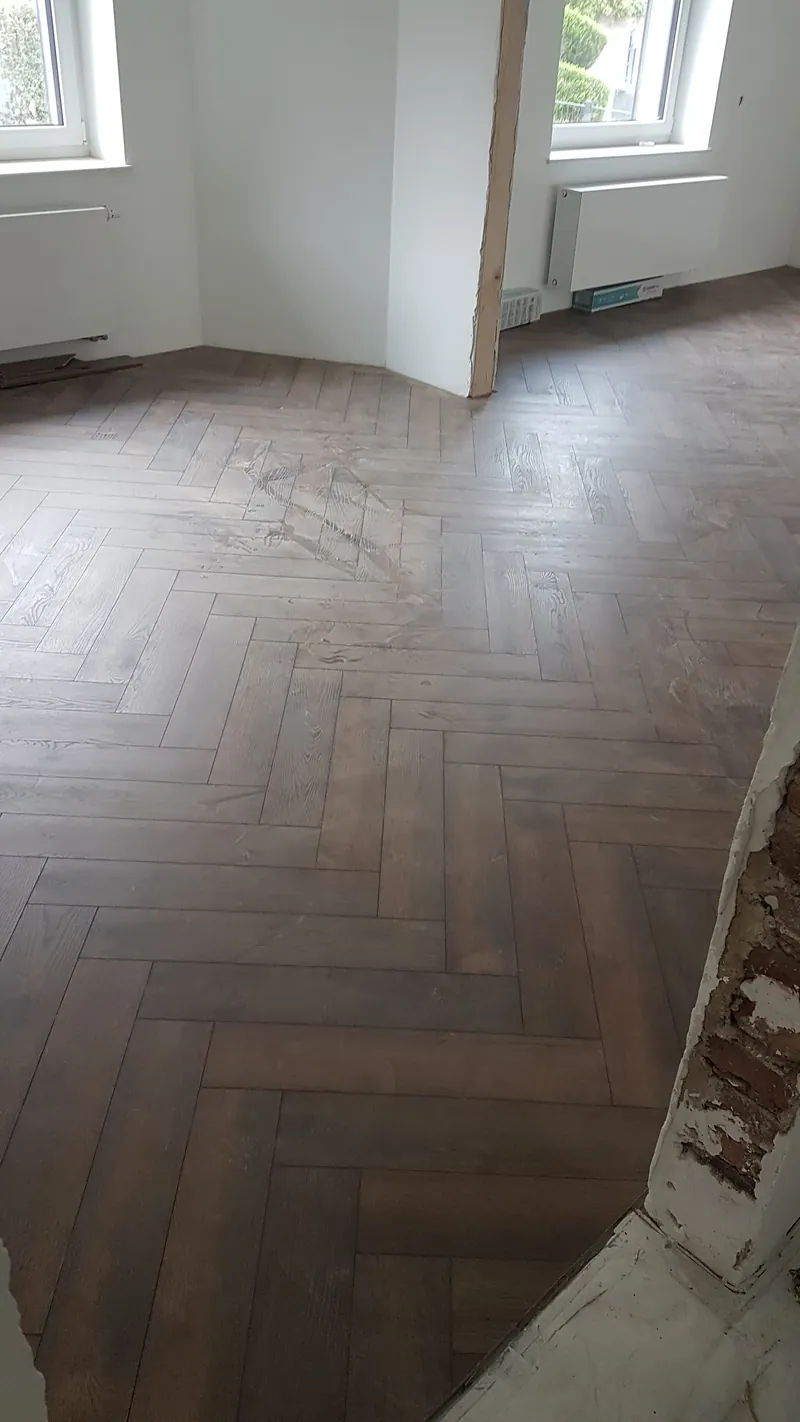 Holzoptik-Fliesen im Fischgrätmuster in einem hellen Raum mit Fenstern