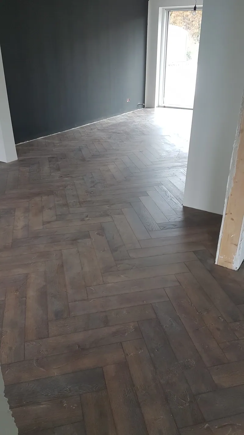Wohnraum mit braunen Holzoptik-Fliesen im Fischgrätmuster und dunkler Wand