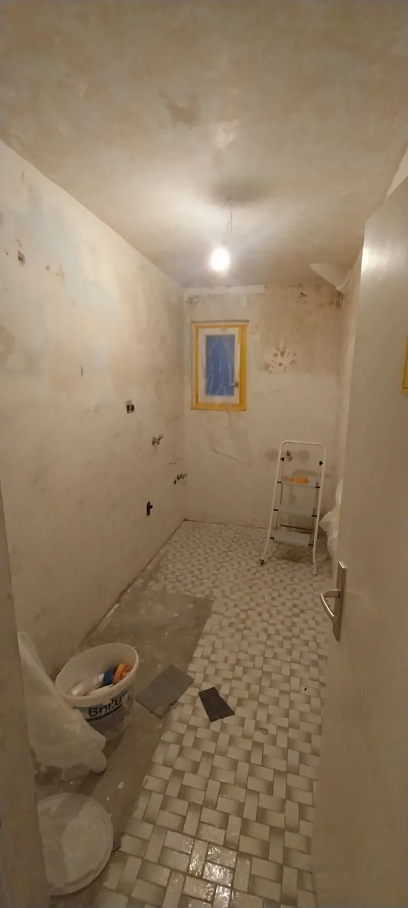 Bad im Umbau mit altem Mosaikfliesenboden, Baustellenlampe und Fensterlaibung