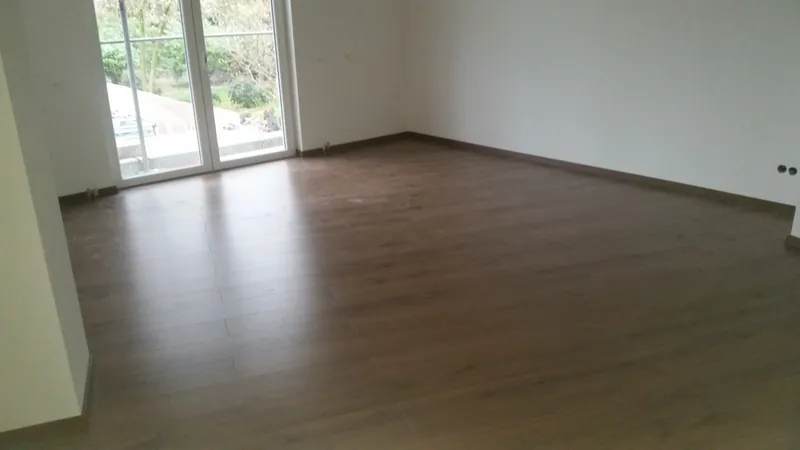 Heller Raum mit Holzoptik-Fliesen und bodentiefen Fenstern
