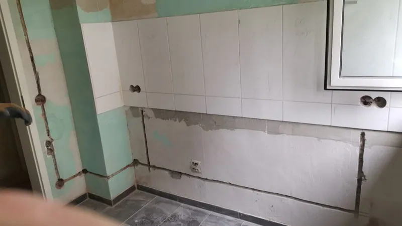 Küchenwand mit Leitungsschlitzen unter alten weißen Fliesen