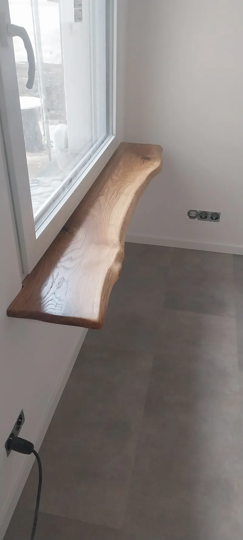 Fensterbank aus Massivholz mit Baumkante unter einem Fenster, grauer Boden