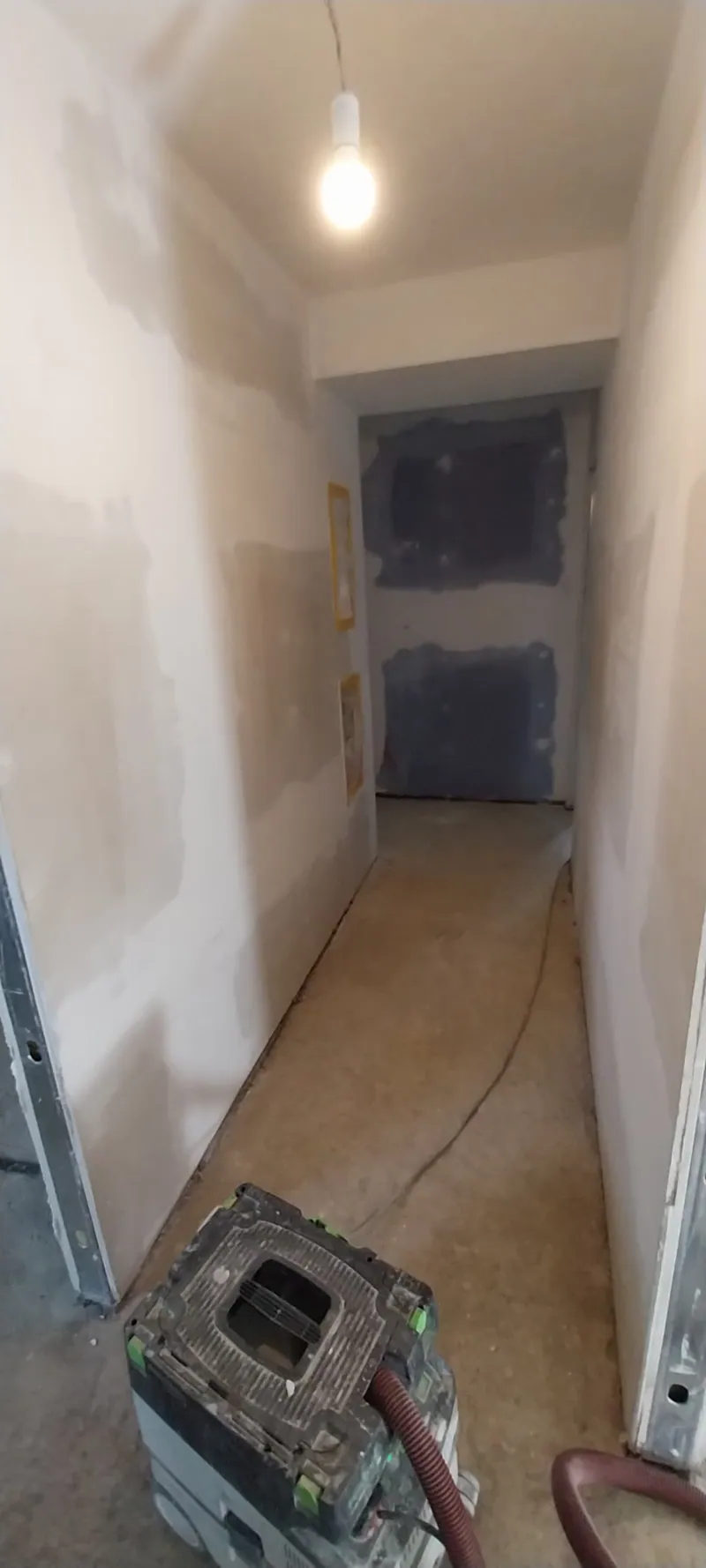 Schmaler Flur mit gespachtelten Trockenbauwänden und Baustellenlampe