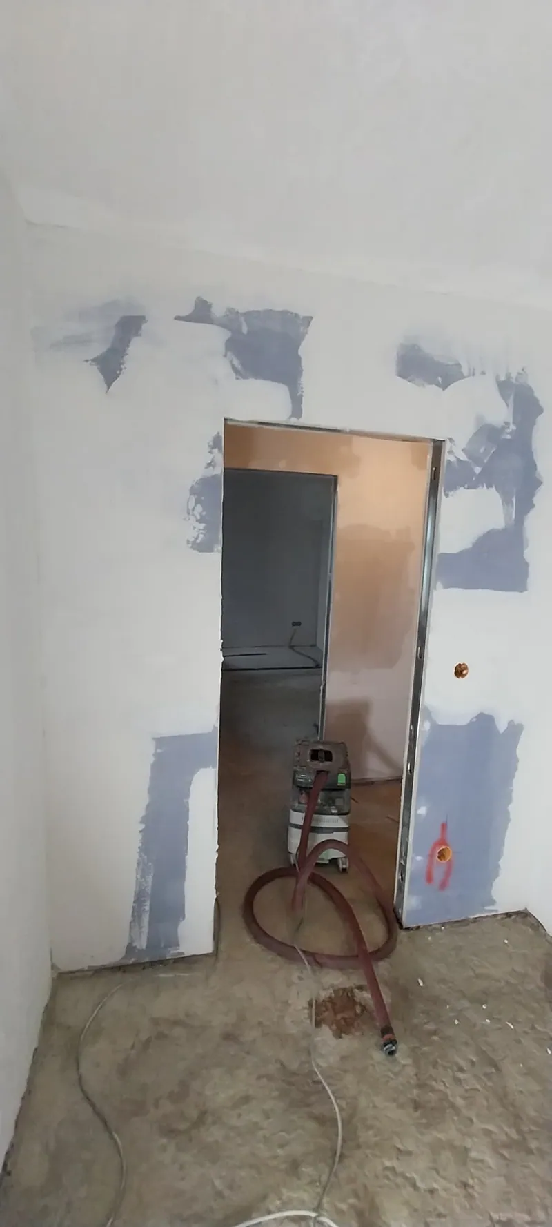 Trockenbauwand mit blau gespachtelten Stellen und Türöffnung, Staubsauger auf dem Boden