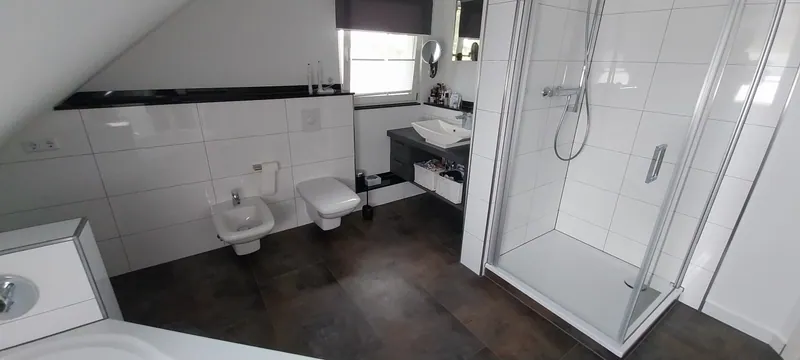 Dachgeschossbad mit weißen Wandfliesen, dunklem Boden, Glasdusche und Wand-WC