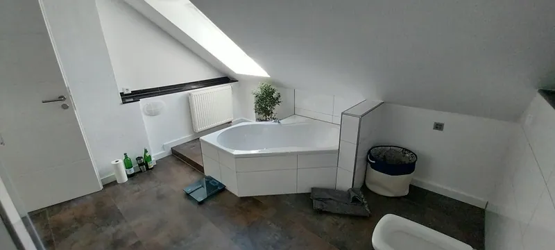 Dachgeschossbad mit weißen Wandfliesen, dunklem Bodenbelag und Eckbadewanne