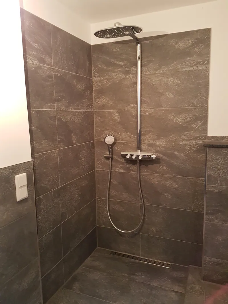 Dusche mit großformatigen braungrauen Wandfliesen, Regendusche und Bodenablaufrinne