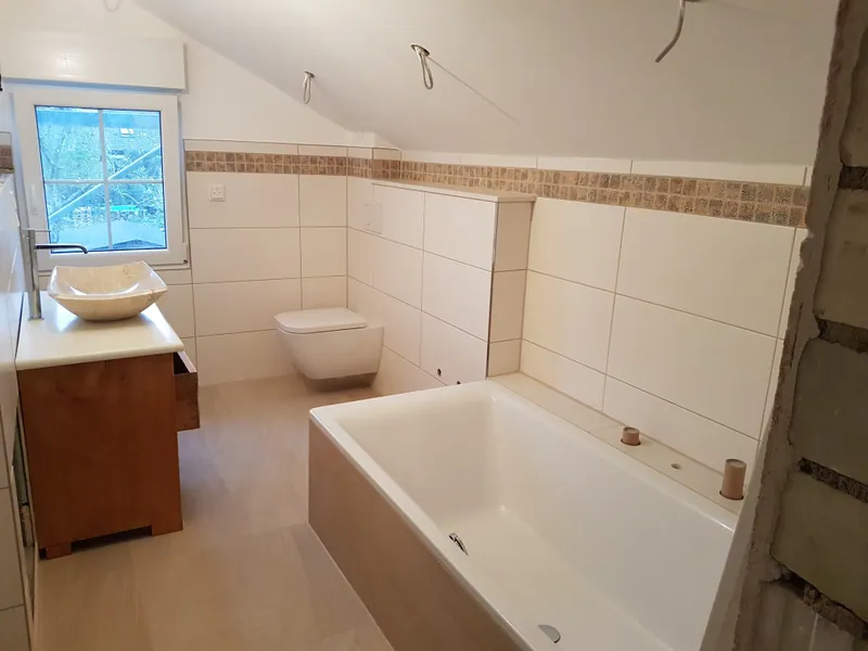 Badezimmer im Rohbau mit weißen Wandfliesen, Mosaikbordüre und eingebauter Badewanne