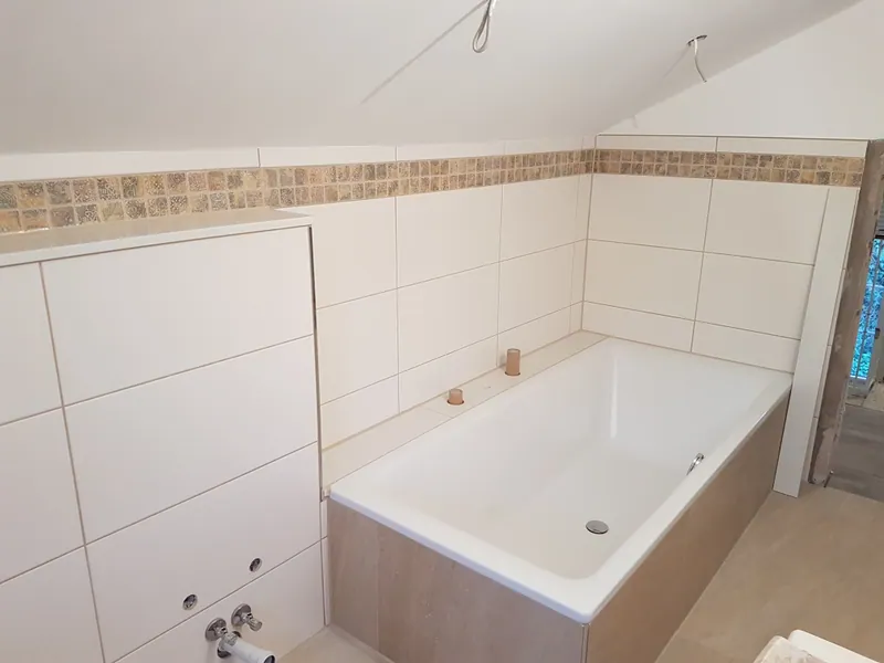 Eingebaute Badewanne mit weißen großformatigen Wandfliesen und Mosaikbordüre im Dachgeschoss