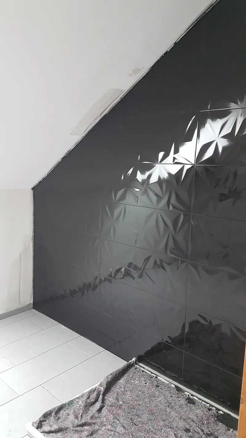 Schwarze Wandfliesen mit Reliefstruktur an einer Dachschräge, davor bodengleiche Dusche