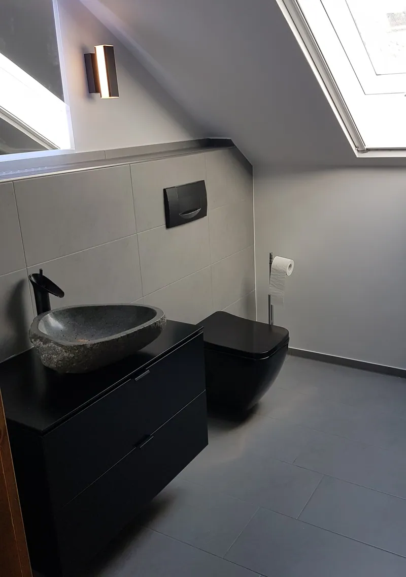 Dachgeschossbad mit grauen Bodenfliesen, Steinwaschbecken und schwarzem Waschtisch