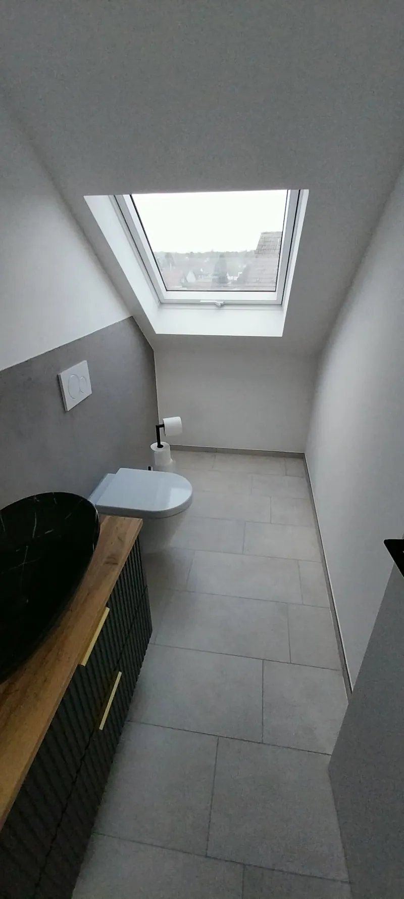 Schmales Dachgeschossbad mit grauen großformatigen Bodenfliesen und Dachfenster