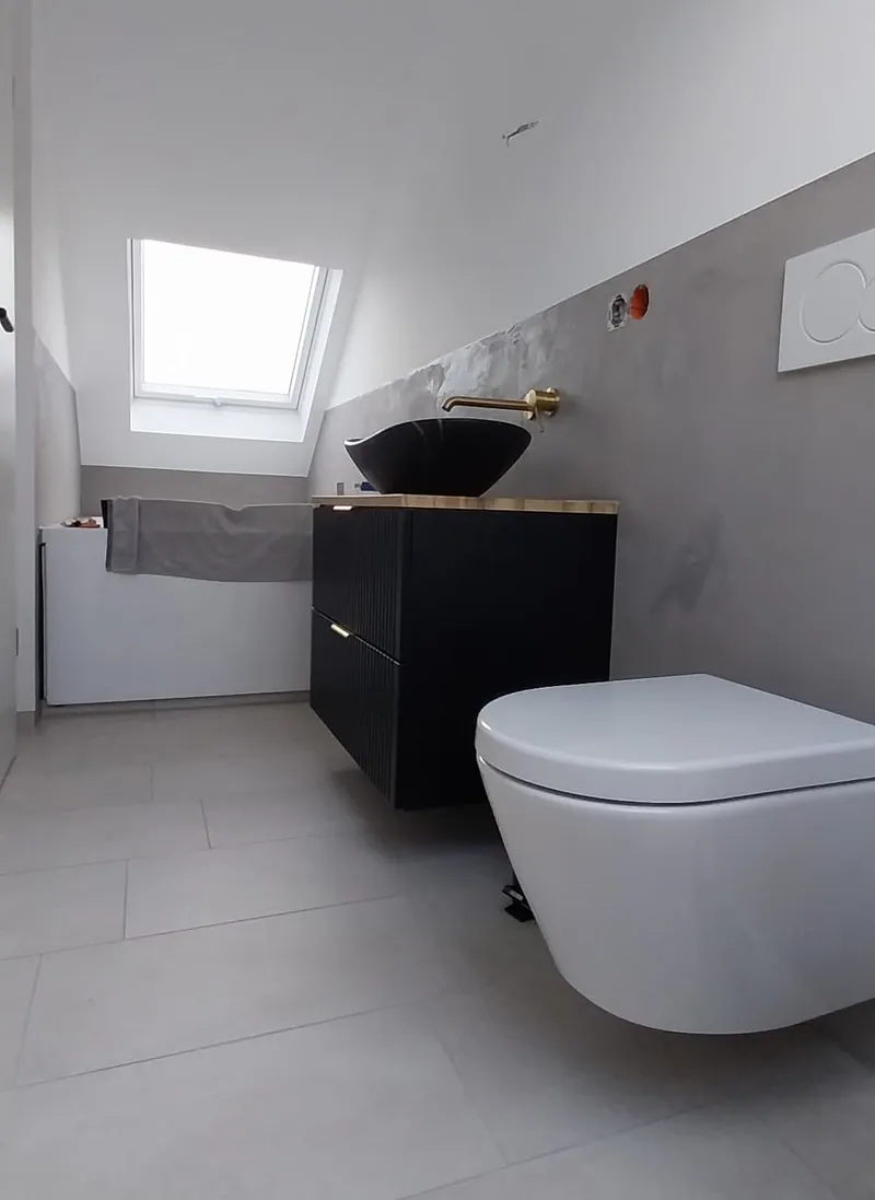 Bad mit hellgrauen großformatigen Bodenfliesen, Wand-WC und schwarzem Waschtisch