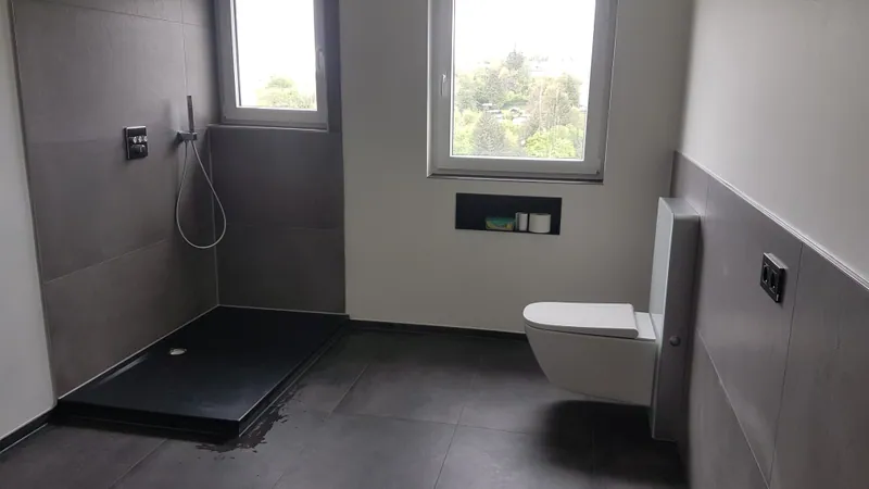 Badezimmer mit dunklen Bodenfliesen, grauen Wandfliesen und bodengleicher Dusche